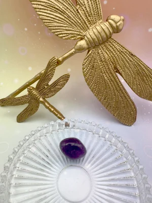 Pierre roulée en améthyste entourée de libellules dorées – symbole de sérénité, de guidance intérieure et de clarté mentale.