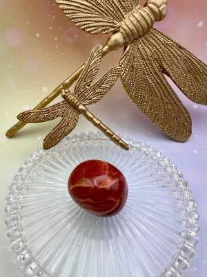 Pierre roulée en jaspe rouge entourée de libellules dorées – symbole de stabilité, de vitalité et de courage