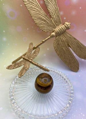 Pierre roulée en oeil de tigre sous des libellules dorées – symbole de protection solaire et d’énergie vitale