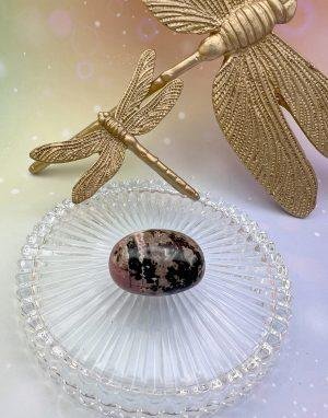 Pierre roulée en rhodonite sous des libellules dorées – symbole d’amour guérisseur et d’équilibre émotionnel